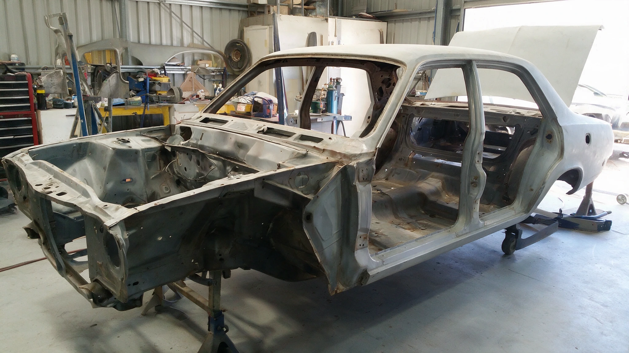 Vintage Australian sedan stripped back to bare metal on a clean workshop floor with panels removed and restoration in progress