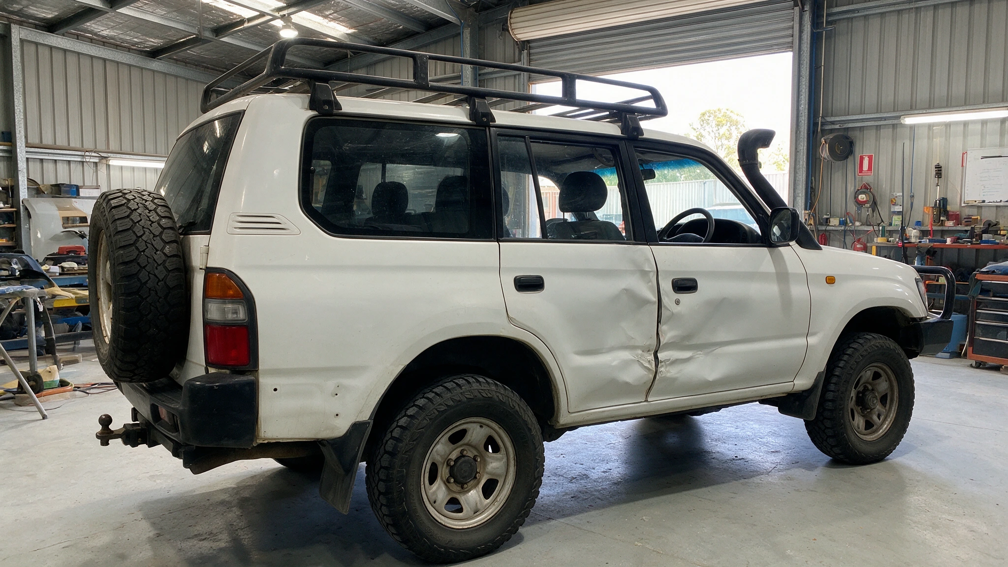4WD with a crease along the driver's door sitting in a clean workshop bay awaiting panel work